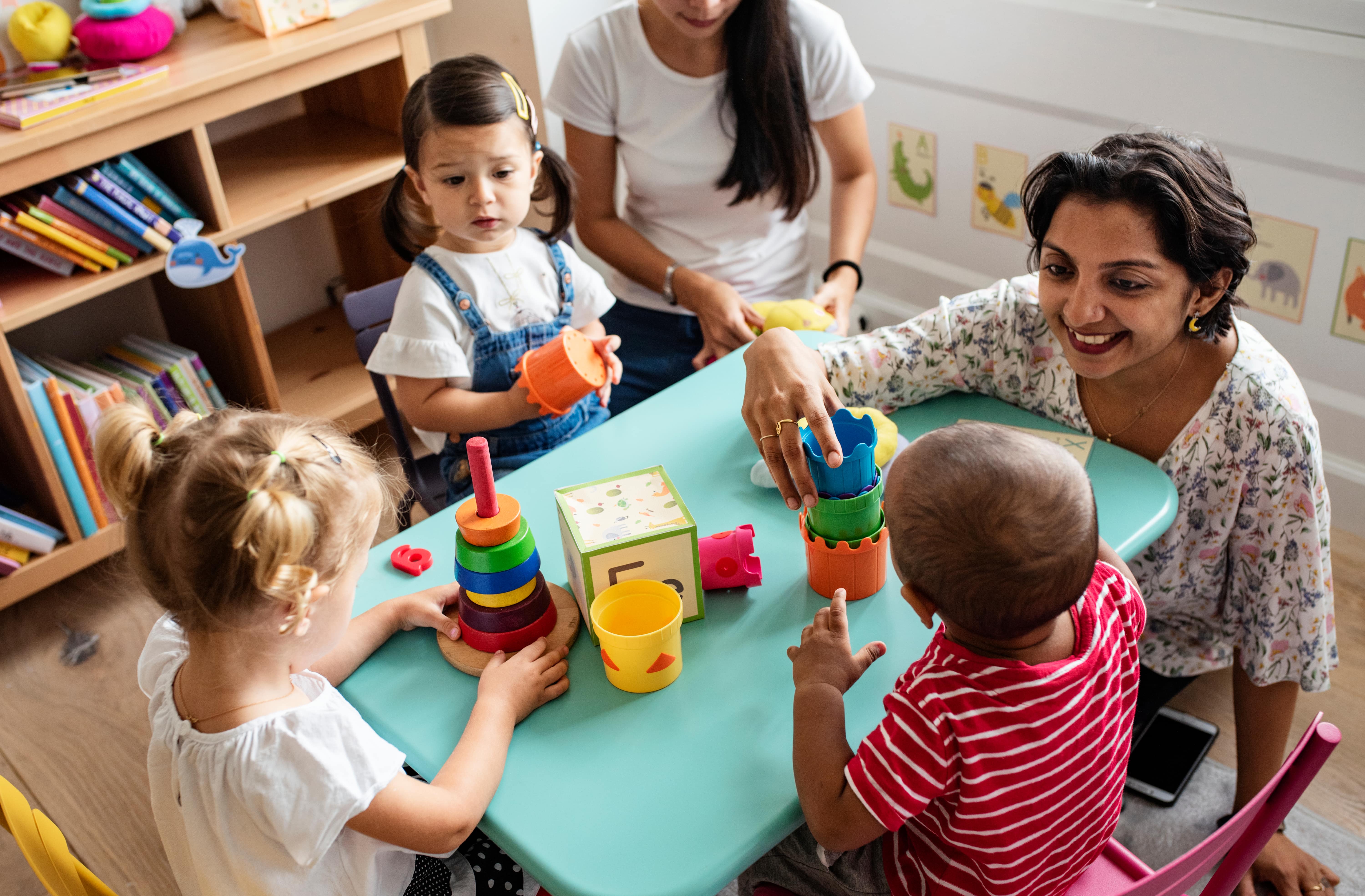 Teacher sitting at the table with young children, playing with blocks. 