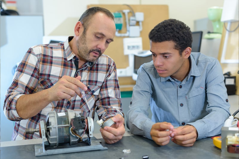 Instructor works with student on repairing mechanical parts. 