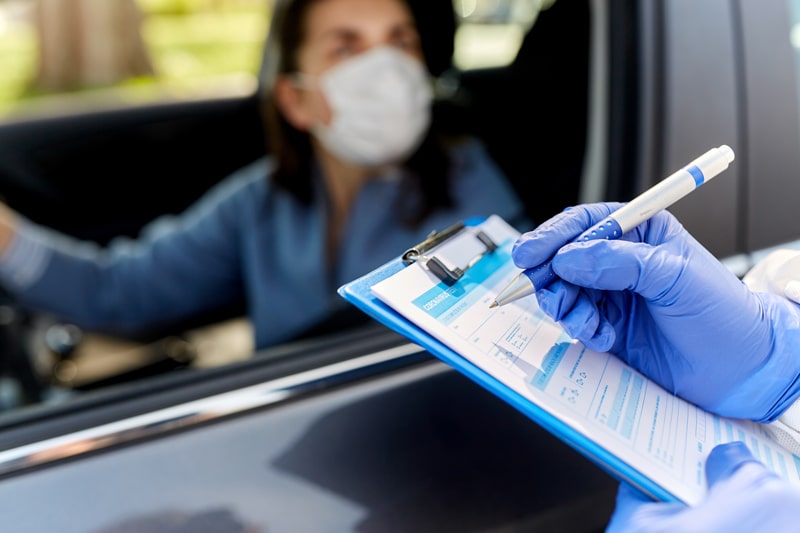 medical person with clipboard talking to patient in car