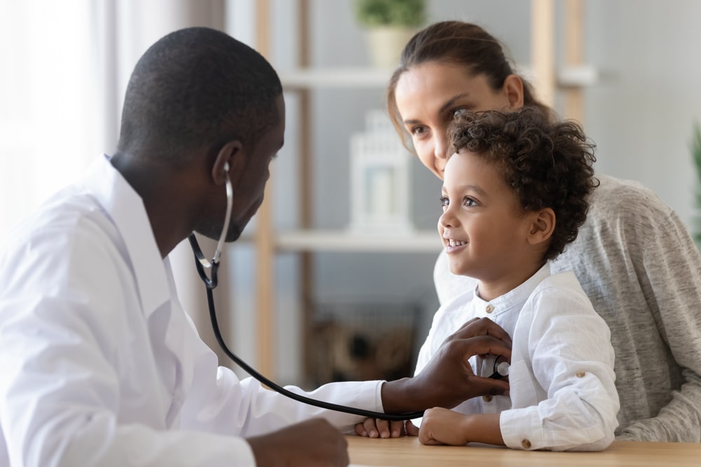 health care worker using stethoscope with toddler on mother's lap.