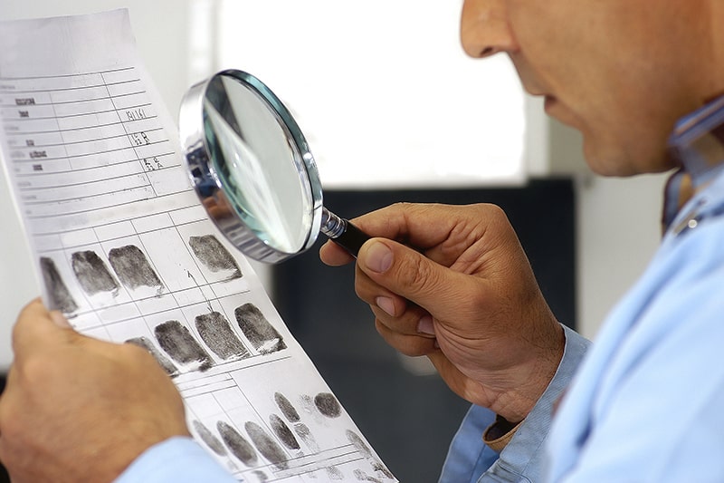 Investigator looking at fingerprints with magnifying glass.