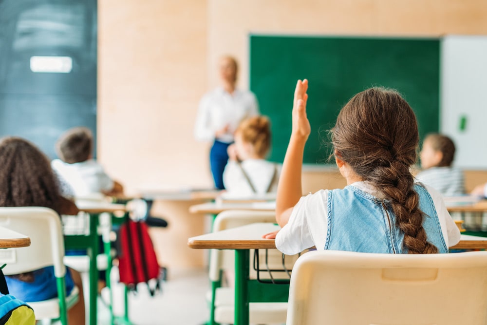elementary girl raising hand in classroom