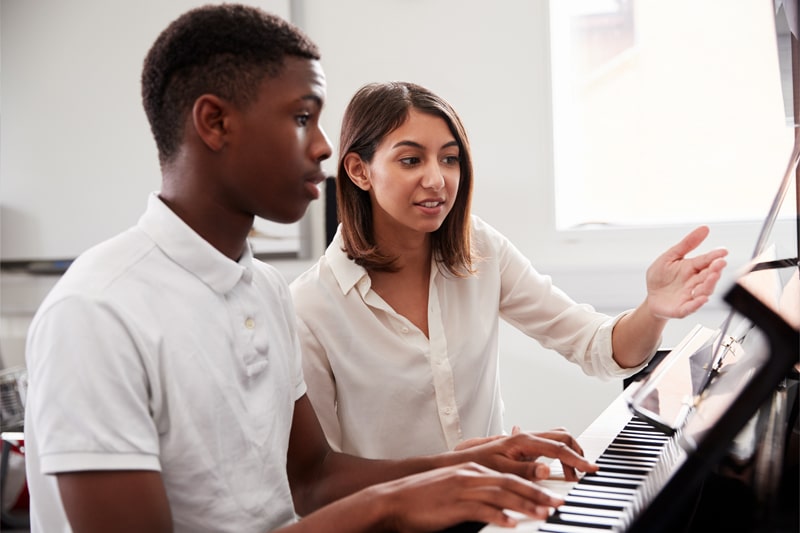 Teacher sits with student at the piano.