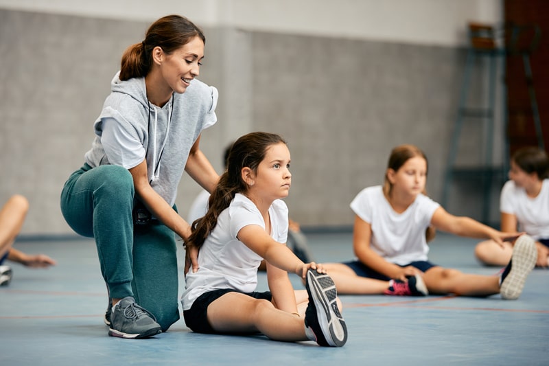 teacher helping school age girl stretching